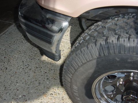 1996 Ford Bronco - Close-up of the front corner of a tan 1996 Ford Bronco, showing the chrome bumper and a large off-road tire.