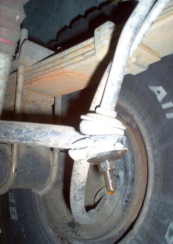 1988 Ford Bronco - Close-up of vehicle suspension components, showing a leaf spring and a bolt with fluid leakage.