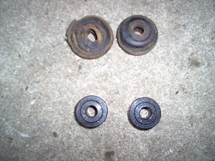 1988 Ford Bronco - Two old, worn leaf spring bushings are shown next to two new ones, likely for a vehicle repair.
