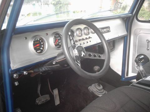 1978 Ford Bronco - Driver's-side interior of a stripped truck cab with a custom brushed-aluminum dash panel holding a large tachometer, speedometer, a row of…