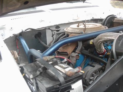 1978 Ford Bronco - Engine bay of a white truck seen from the passenger side, showing a blue-painted V8 with a large round air cleaner, braided stainless hose,…
