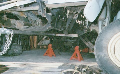 1978 Ford Bronco - The undercarriage of a 1978 Ford Bronco is visible, supported by jack stands, with apparent frame damage.
