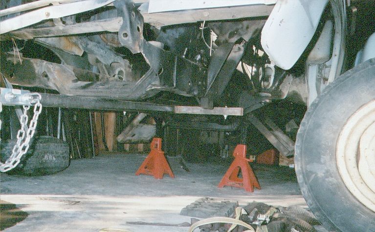 Underside of a light blue truck on orange jack stands, frame and steering linkage exposed
