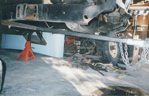 1978 Ford Bronco - The underside of a vehicle is shown supported by jack stands and secured with chains, indicating it is undergoing maintenance or repair.