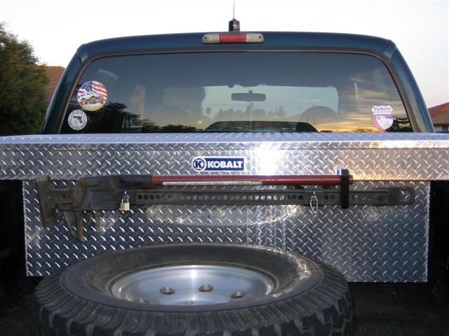 Diamond-plate Kobalt crossbed toolbox with a padlocked Hi-Lift jack and spare tire in a pickup bed