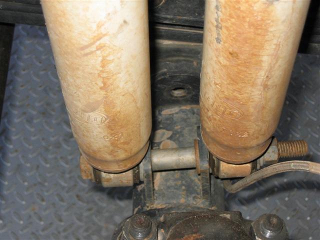 Close-up of two dirty rear shock absorbers with some markings visible