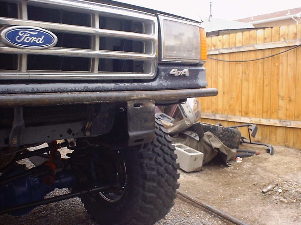 Ford grille with blue oval badge and 4x4 emblem, custom tube bumper, large tire, and suspension parts visible