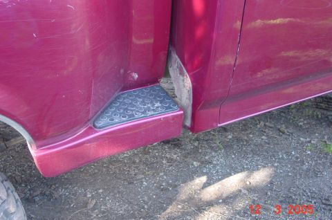 1992 Ford F-150 - Close-up of a red truck's side step and lower body panel, revealing wear and tear.