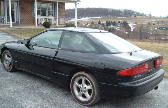 Black 1994 Ford Probe coupe parked on gravel driveway, rear 3/4 view
