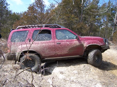 1999 Jeep TJ - Mud-covered SUV tackles challenging off-road trail with steep inclines.