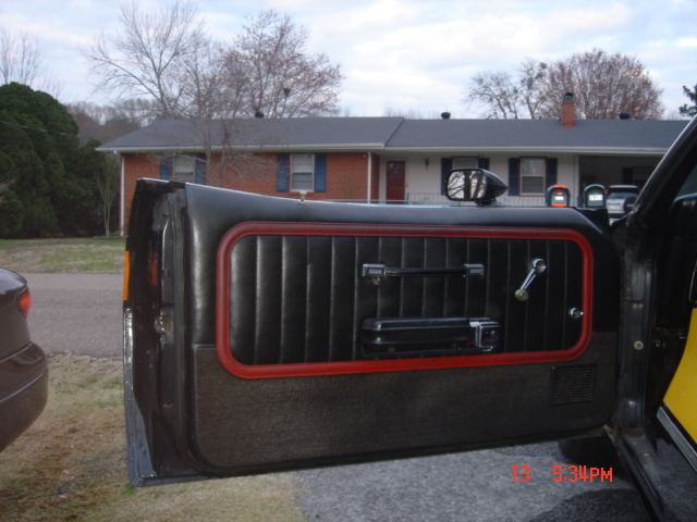 Open truck door with black panel and red-trimmed window, parked in front of brick ranch house