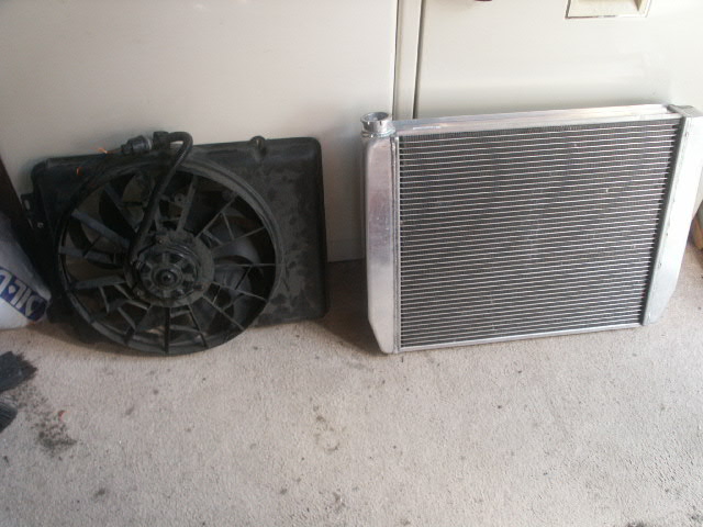 Black electric fan shroud beside a bare aluminum radiator on a carpeted floor.