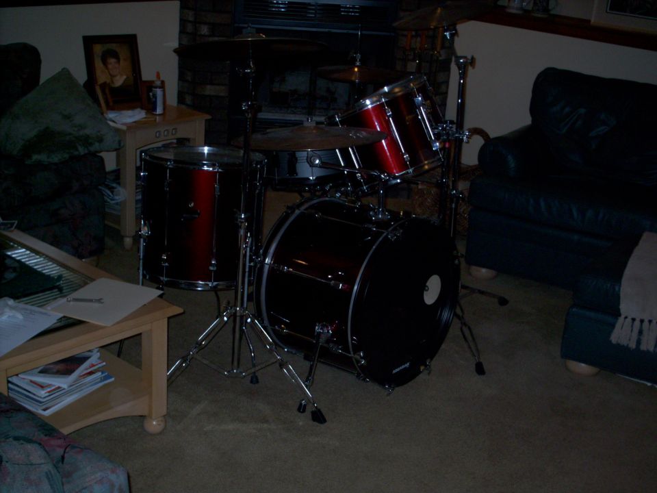 Drum set with red and black drums in a living room, next to a couch and a table with magazines