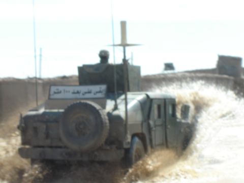 1989 Ford Bronco - A military vehicle navigates through a watery terrain, kicking up a large spray.