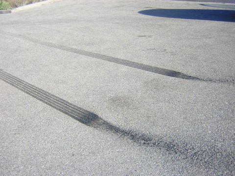1992 Ford Crown Victoria - Pair of fresh black burnout tire marks laid down in parallel stripes across sunlit gray asphalt; no vehicle is in the frame.