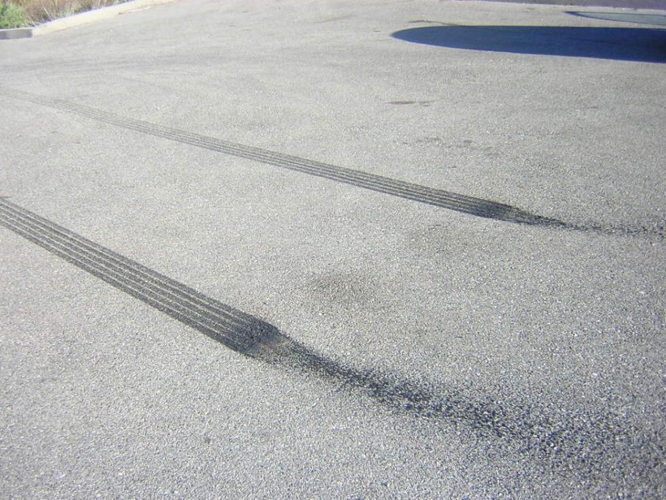 Two parallel black burnout tire marks on gray asphalt
