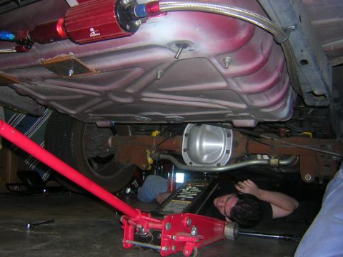 1992 Ford Crown Victoria - Mechanic works on the underside of a vehicle, focusing on the fuel system and rear axle components.