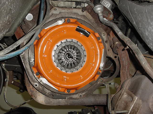 Orange clutch housing and flywheel assembly bolted to engine block, with surrounding metal components