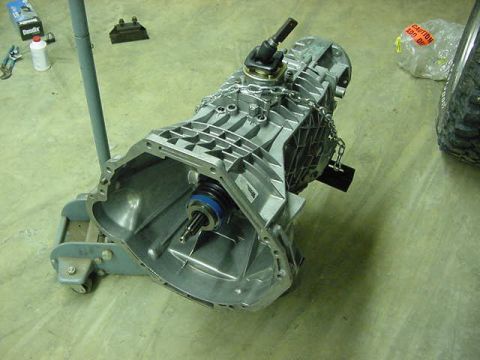 1995 Ford Bronco - A transmission assembly is shown on a jack stand, with various tools and a tire in the background.