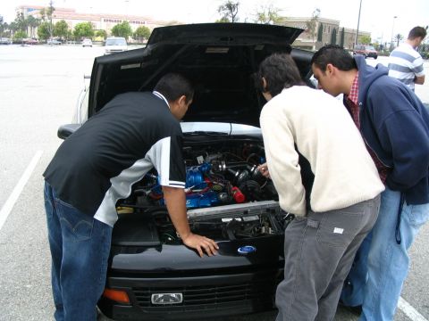 1995 Ford Probe - Several people gather around to inspect the engine bay of a car.
