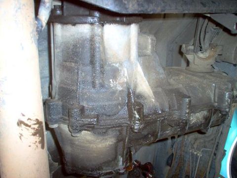 1988 Ford Bronco - Underside view of a heavily soiled transfer case, showing its complex mechanical components and assembly.