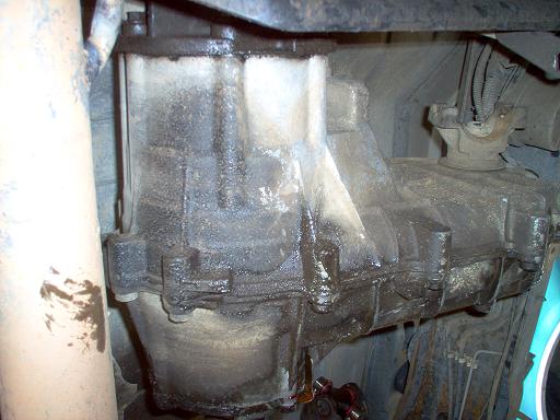 Muddy aluminum transfer case seen from underneath a truck, still bolted in place