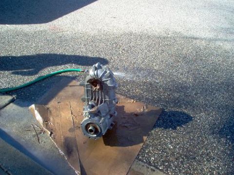 1988 Ford Bronco - Transfer case being cleaned with a garden hose on a paved surface.