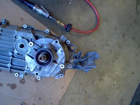 1988 Ford Bronco - A disassembled transfer case sits on a surface, with an air-powered tool and a blue rag next to it.