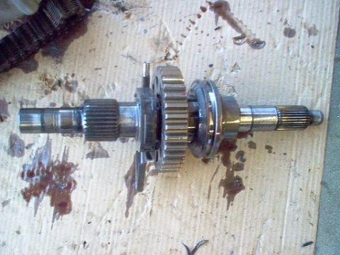 1988 Ford Bronco - Close-up of a disassembled transfer case, showing gears and shafts on a stained surface.