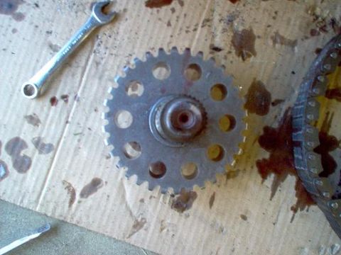 1988 Ford Bronco - A close-up view of a transfer case gear and chain, alongside a wrench on a stained cardboard surface.
