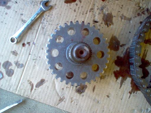 Splined drive sprocket and chain on oily cardboard next to a combination wrench during teardown