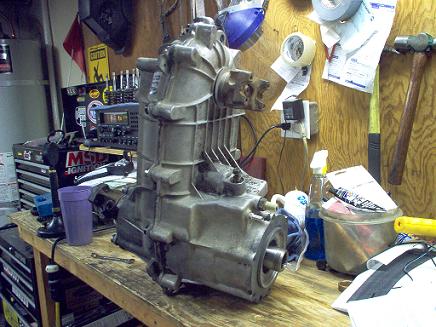 1988 Ford Bronco - A disassembled transfer case rests on a wooden workbench, surrounded by tools and garage clutter.