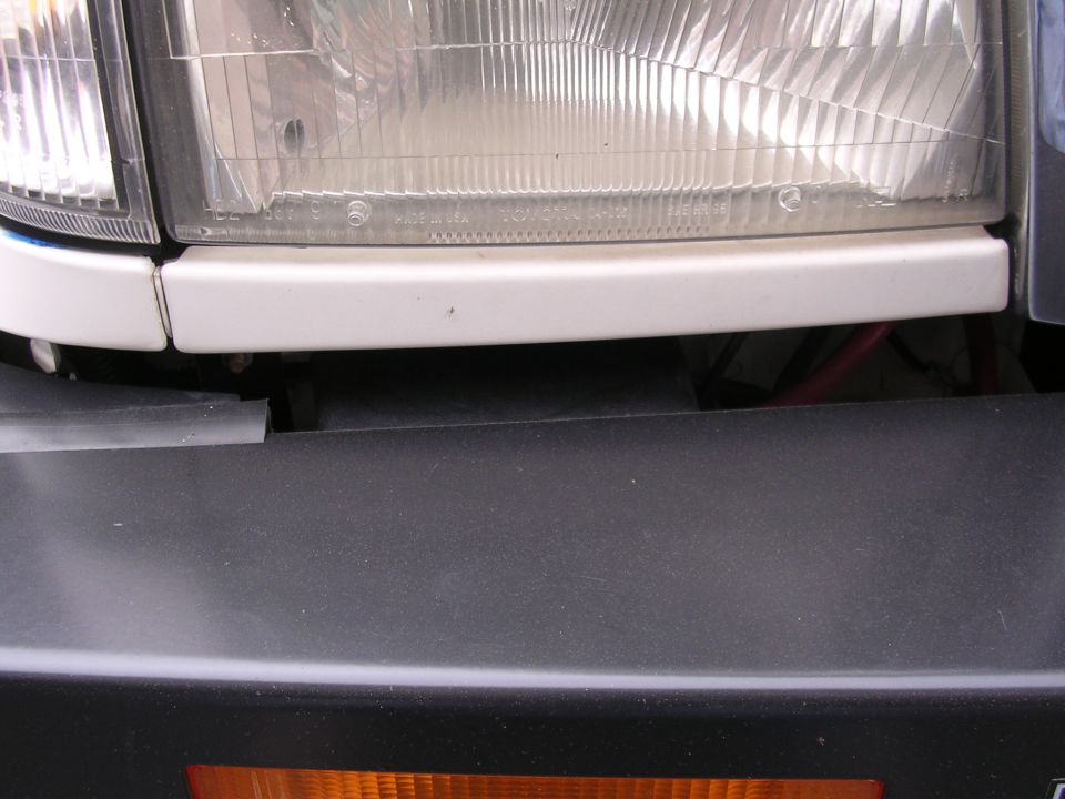 Close-up of a vehicle's headlight and part of the bumper. Text on the headlight reads 'MADE IN USA' and 'TOYOTA MOTOR CORP'