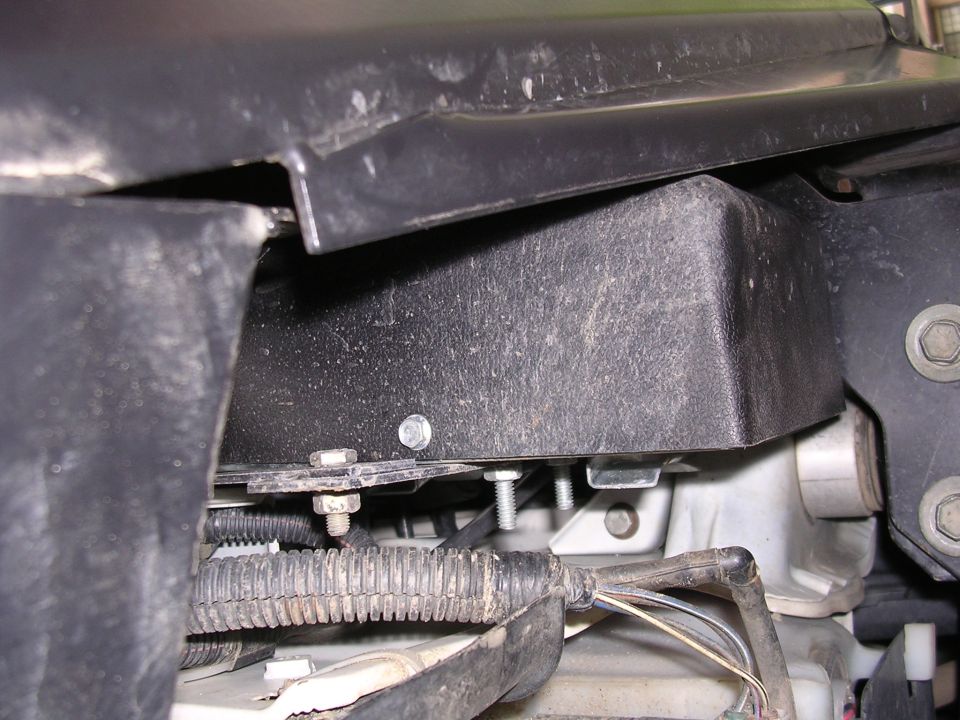 Undercarriage view of vehicle wiring and black plastic housing with visible bolts