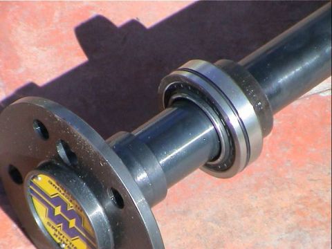 1979 Ford Bronco - Close-up of an axle shaft assembly with a visible hub flange and bearing, a yellow and purple emblem.