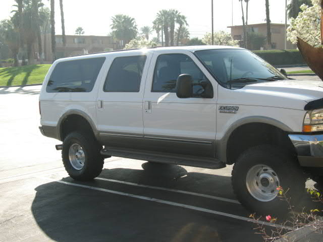 Lifted white and tan Ford Excursion on all-terrain tires in a palm-lined lot