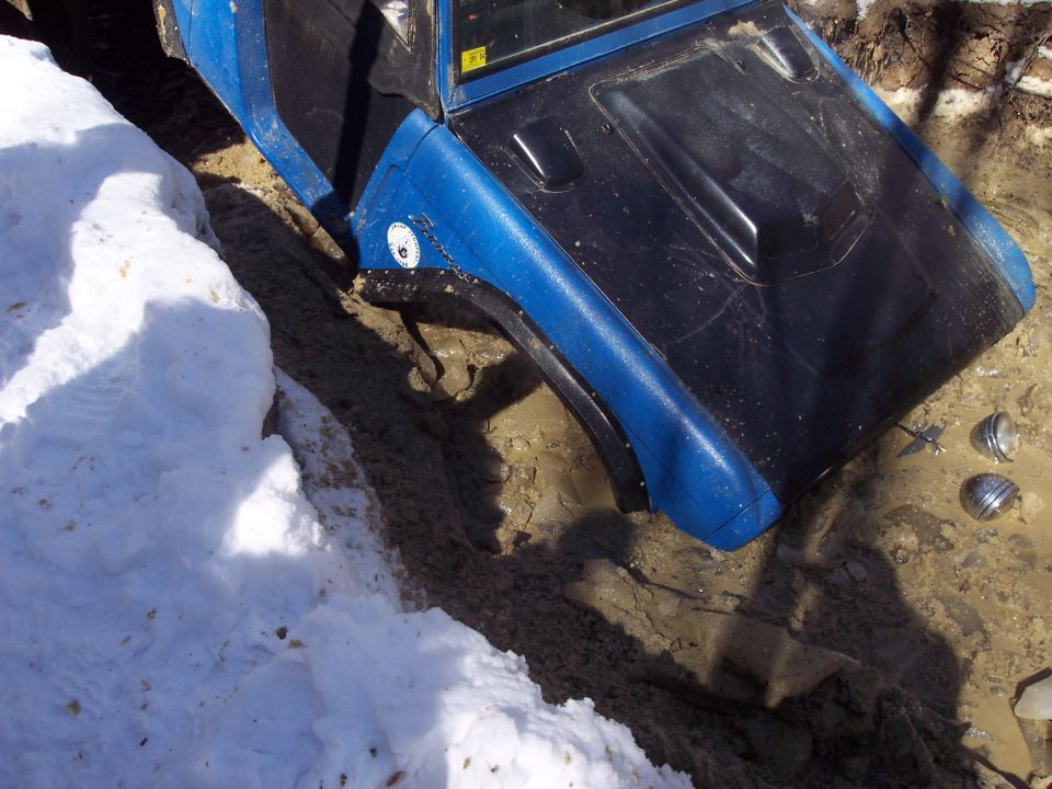 Blue off-road vehicle with black hood stuck in mud and snow, front wheel partially visible