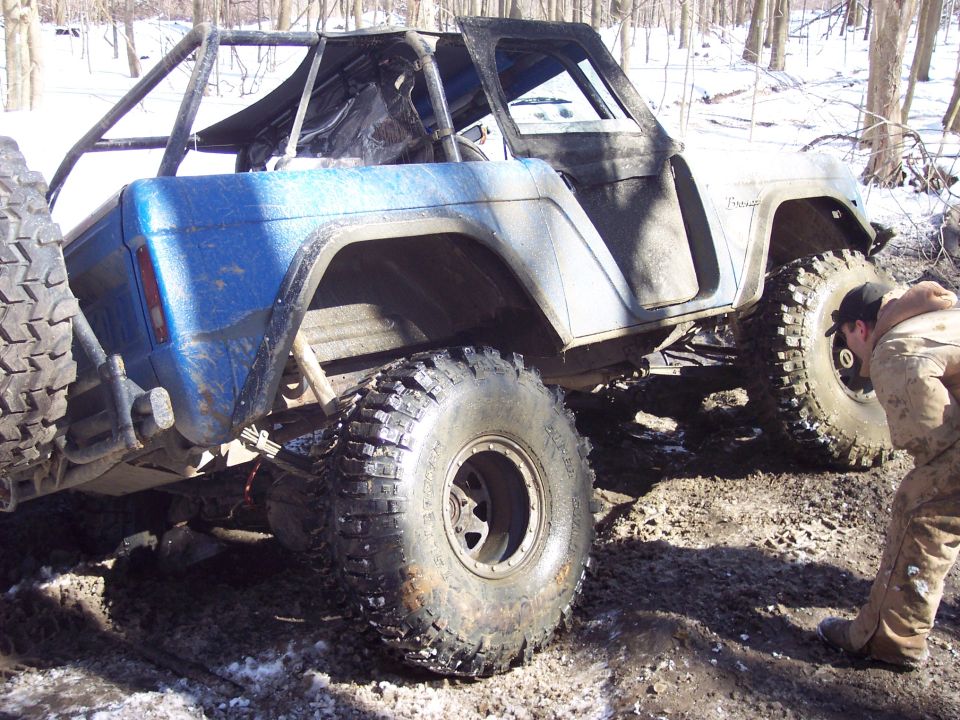 Blue and white 1974 Ford Bronco with roll cage and large tires in muddy terrain