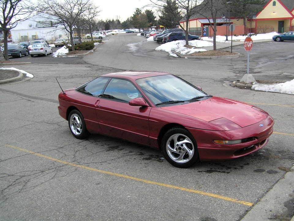 Red 1993 Ford Probe coupe with chrome wheels parked in a snowy parking lot, 3/4 front view