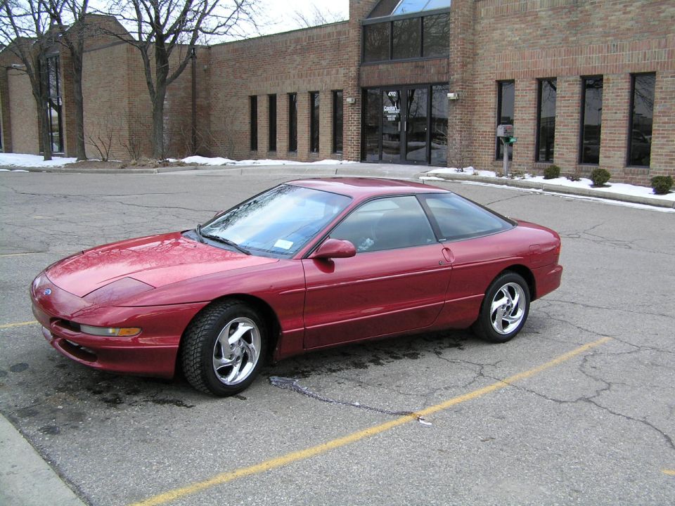 Red Ford Probe coupe parked in a lot in front of a brick office building with snow patches