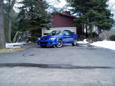 2003 Mazda Protege - A blue 2003 Mazda Protege sedan is parked in a driveway in front of a house.