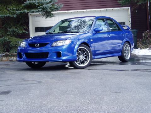 2003 Mazda Protege - A blue 2003 Mazda Protege sedan is parked in front of a garage.