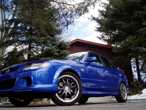 2003 Mazda Protege - A blue 2003 Mazda Protege sedan with custom wheels and body kit is parked in front of a house.