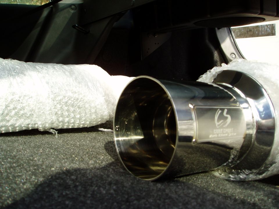 Chrome exhaust tip with engraved CS logo lying in bubble wrap inside a car trunk