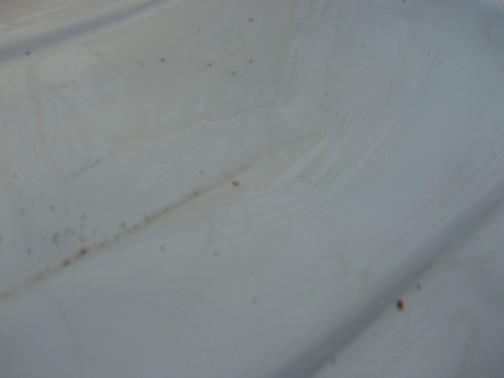 Close-up of white fiberglass or painted surface with small rust spots and dirt streaks