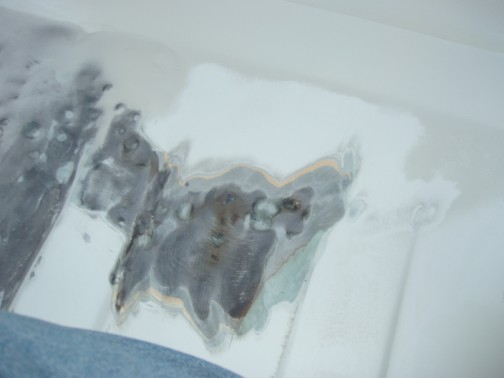 Close-up of sanded white body panel showing bare metal, rust spots and filler during body repair