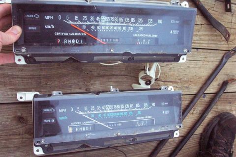 1985 Ford LTD Crown Victoria - Two automotive instrument clusters are displayed on a wooden surface.