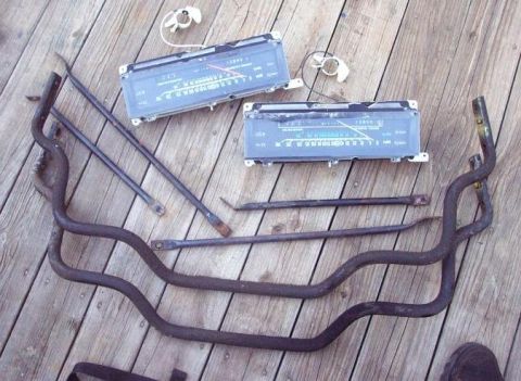 1985 Ford LTD Crown Victoria - Various car parts, including two dashboard instrument clusters and metal rods, are laid out on a wooden deck.