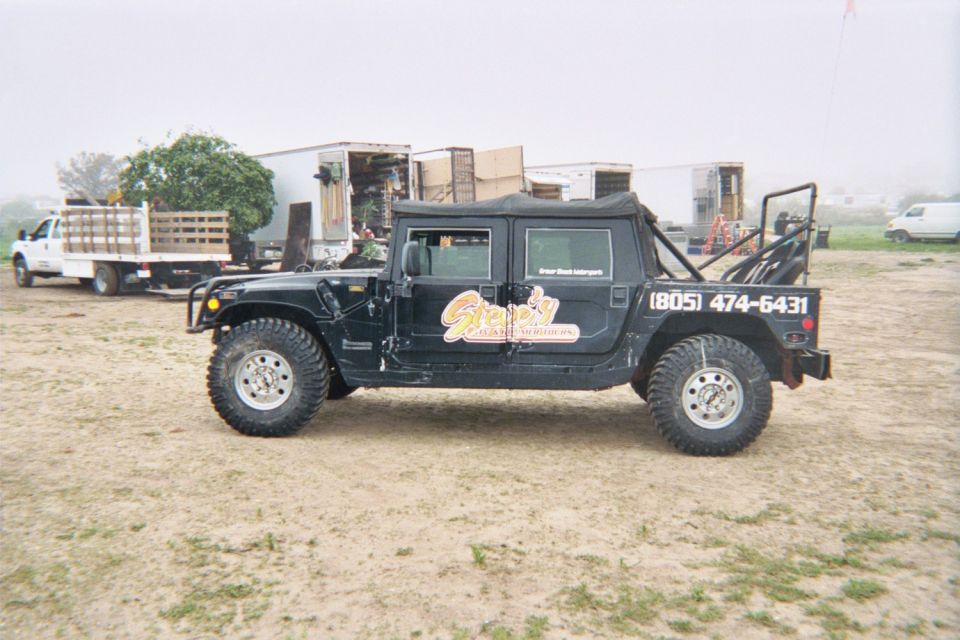 Black soft-top Hummer with shop lettering parked in a dirt lot