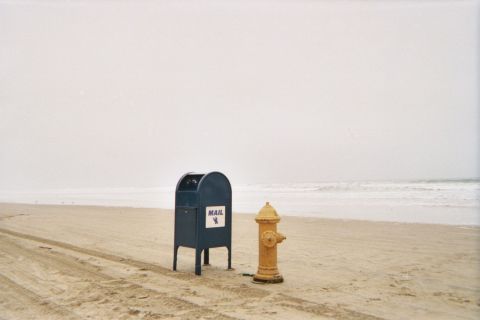 1990 Ford Bronco - blue mail collection box and a yellow fire hydrant stand incongruously side by side on an empty foggy beach near the surf.